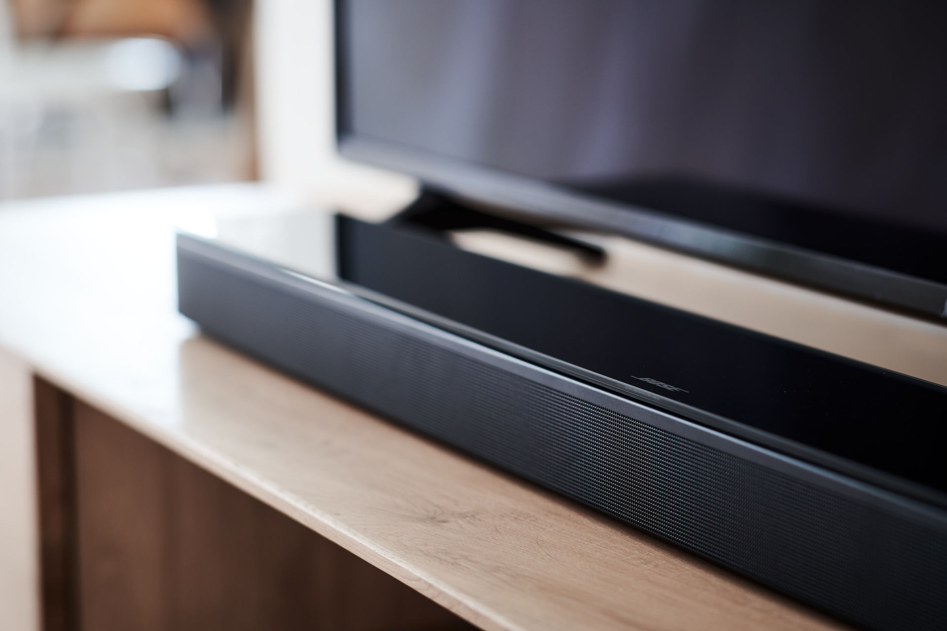 Schwarze Soundbar auf einem Holzschrank, vor einem Fernseher.