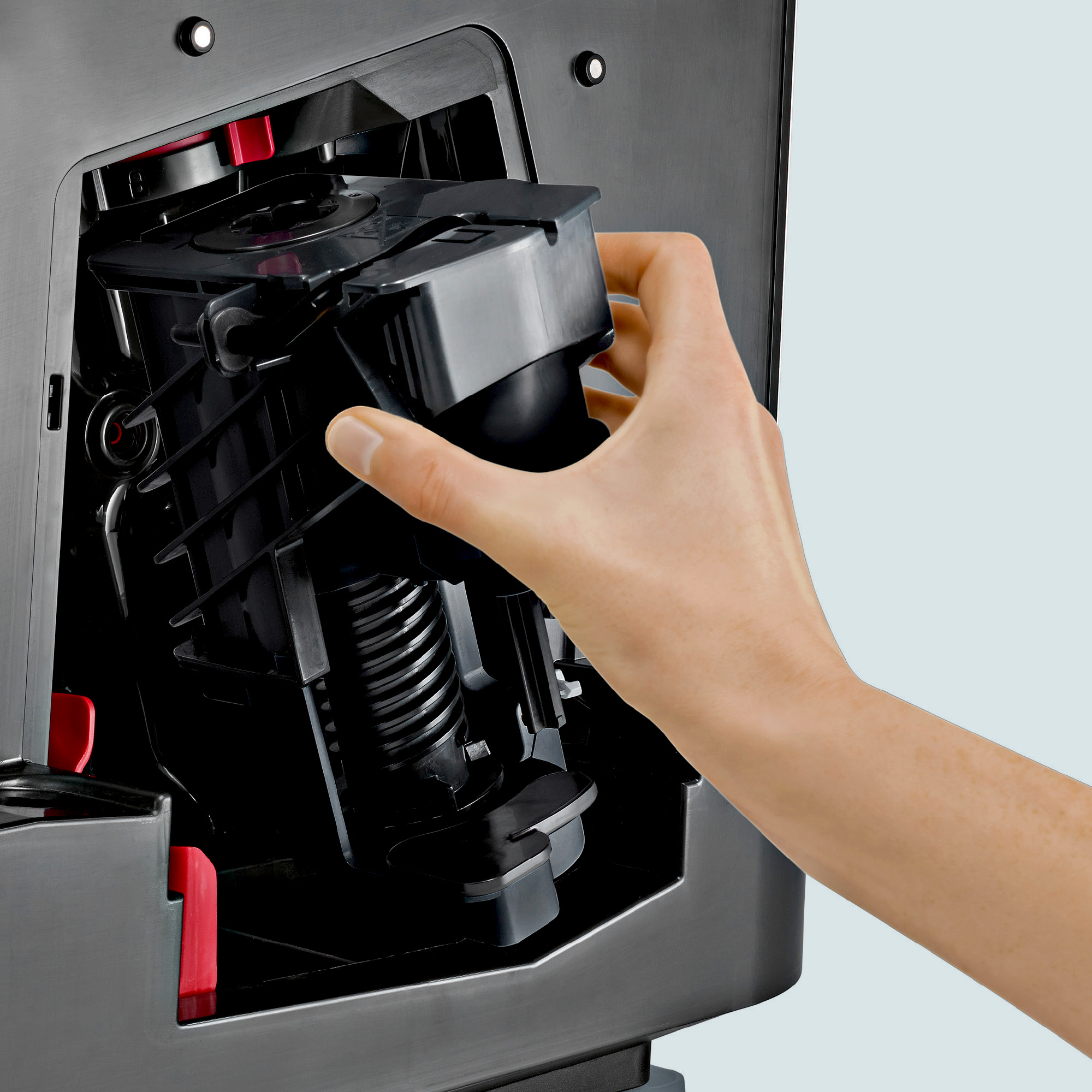 Hand setzt eine schwarze Komponente in eine dunkle Kaffeemaschine ein.