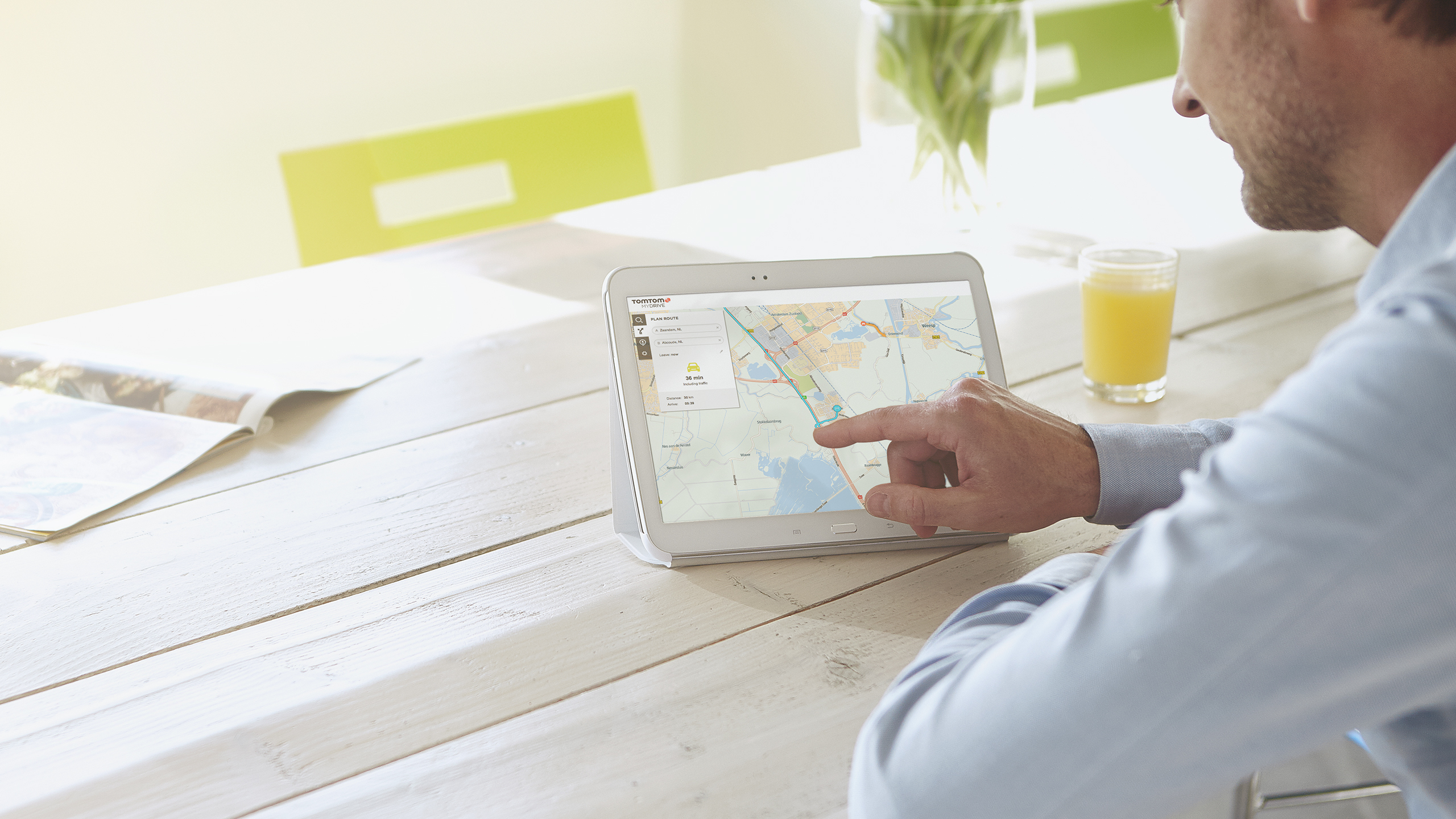 Un hombre usando una tableta con un mapa en una mesa de madera blanca. Zumo de naranja.
