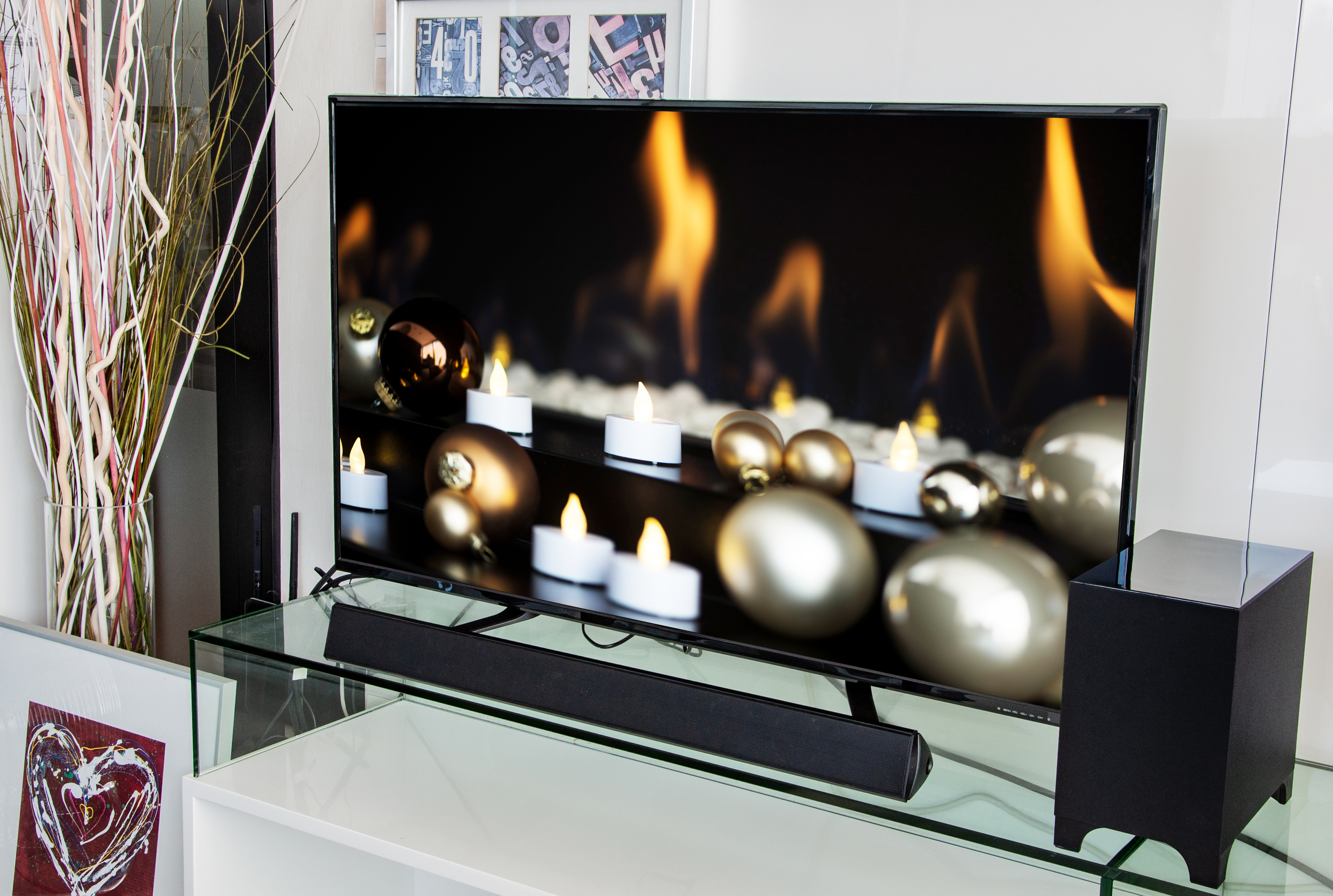 Wohnzimmer-Szene mit einem Fernseher, der Kerzen und Ornamente zeigt, und einer Soundbar.