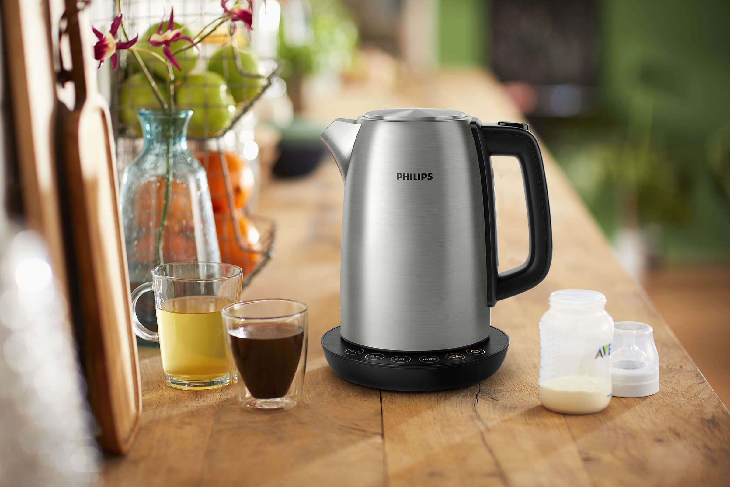 Silberner Philips Wasserkocher auf schwarzem Sockel, mit Gläsern und Vase auf Tisch.