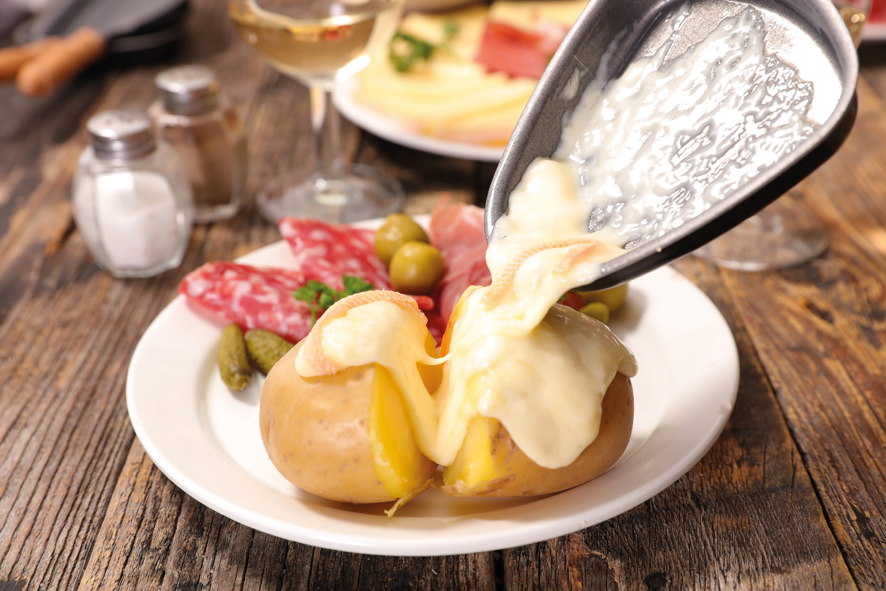 Raclette-Gericht mit geschmolzenem Käse über Kartoffeln, Salami, Oliven und Essiggurken.