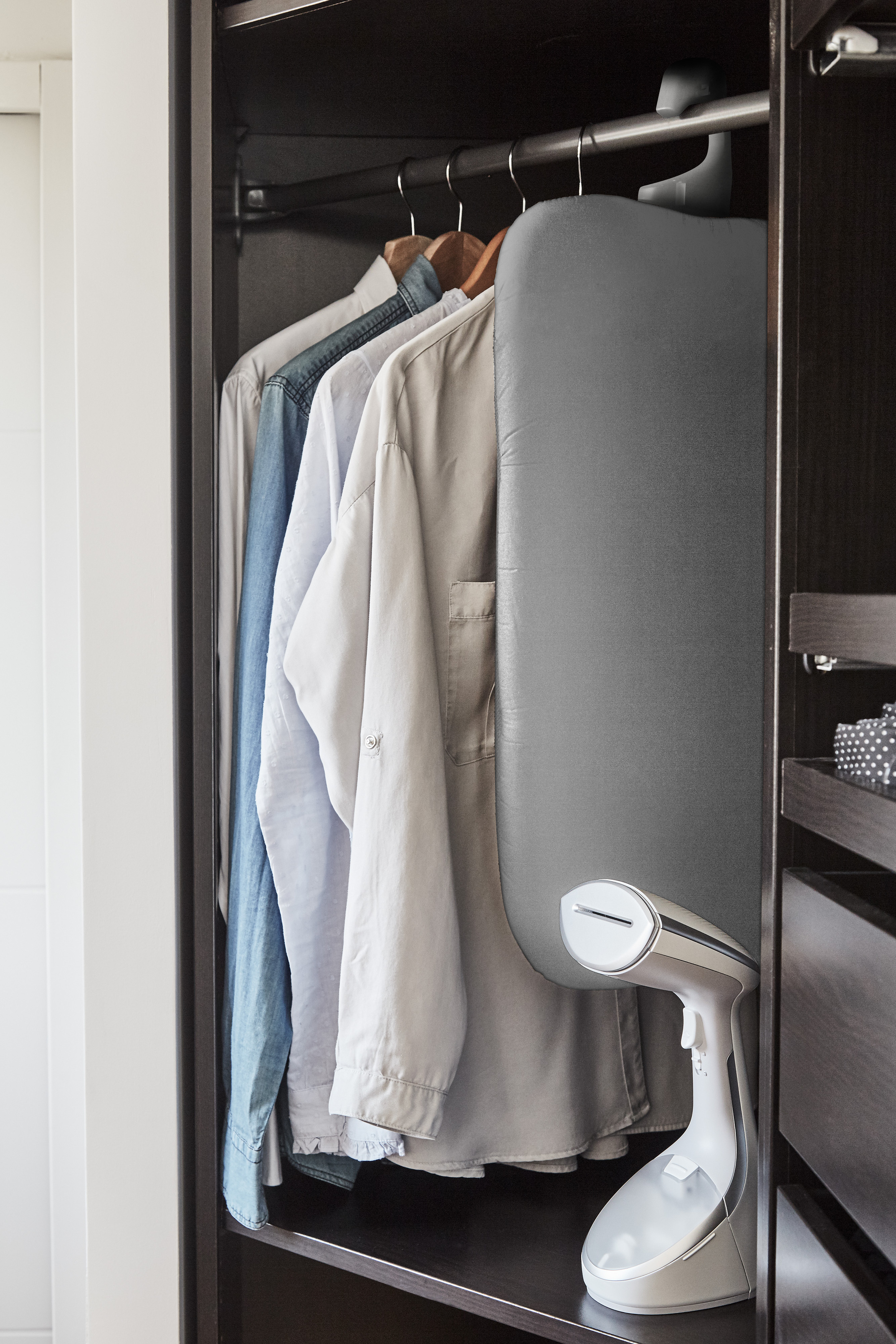 Kleiderschrank mit Hemden, einem Bügelbrett und einem Dampfgarer.