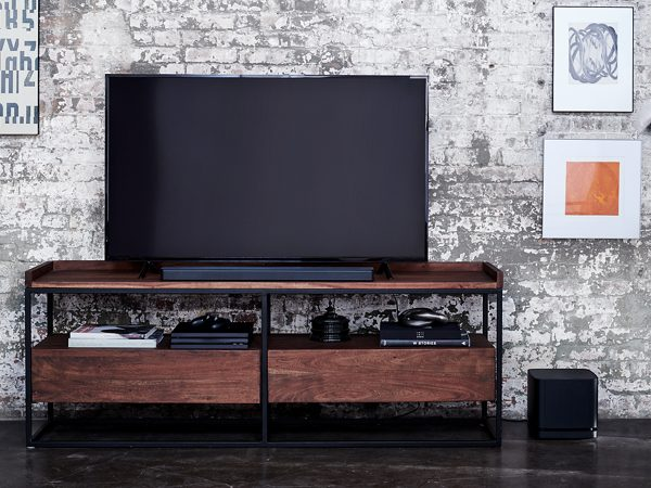 Living room scene with TV, soundbar, and storage on a dark wooden stand. Brick wall.