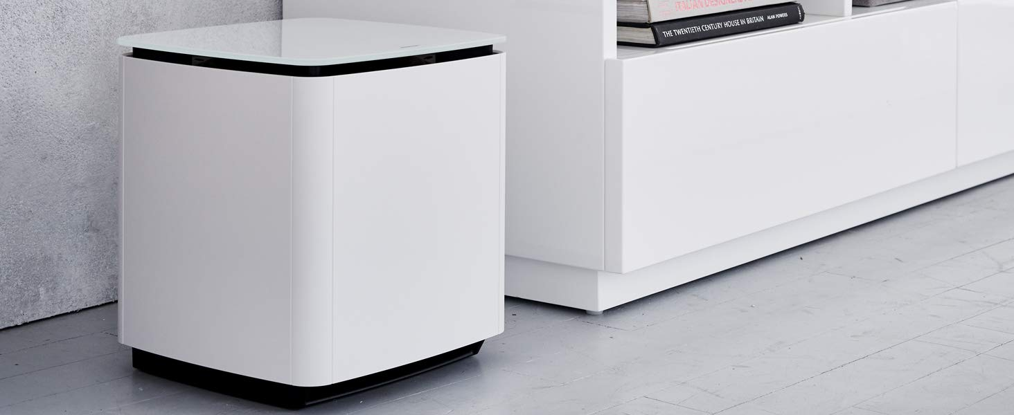 A white subwoofer next to a white cabinet and a wall.