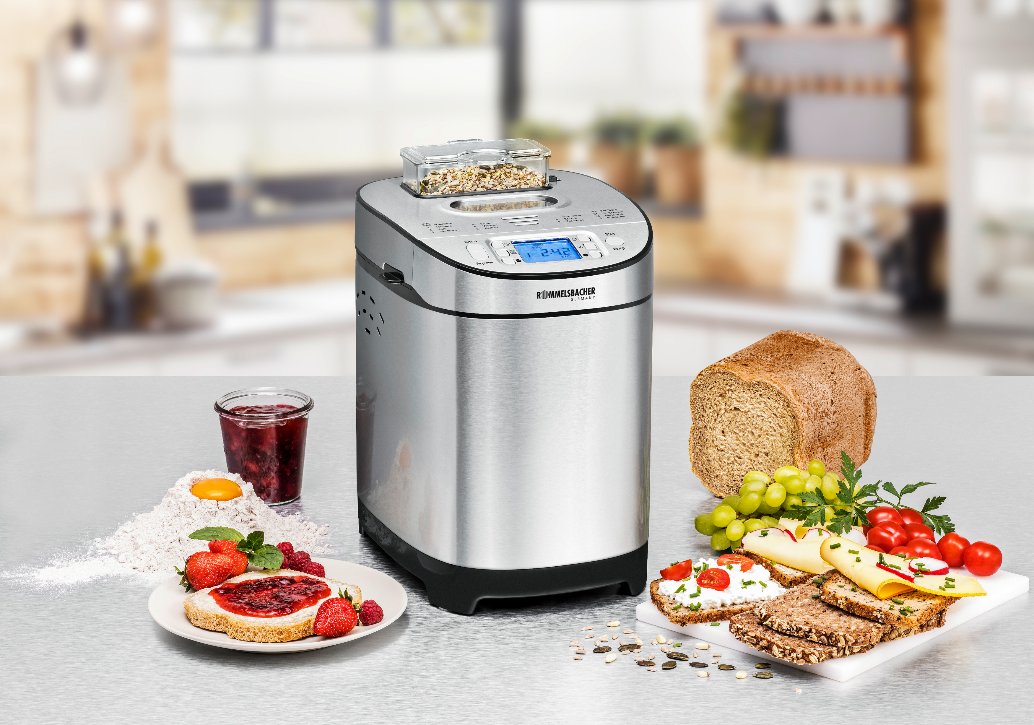 Ein silberner Brotbackautomat mit Lebensmitteln wie Brot, Obst und Aufstrichen.