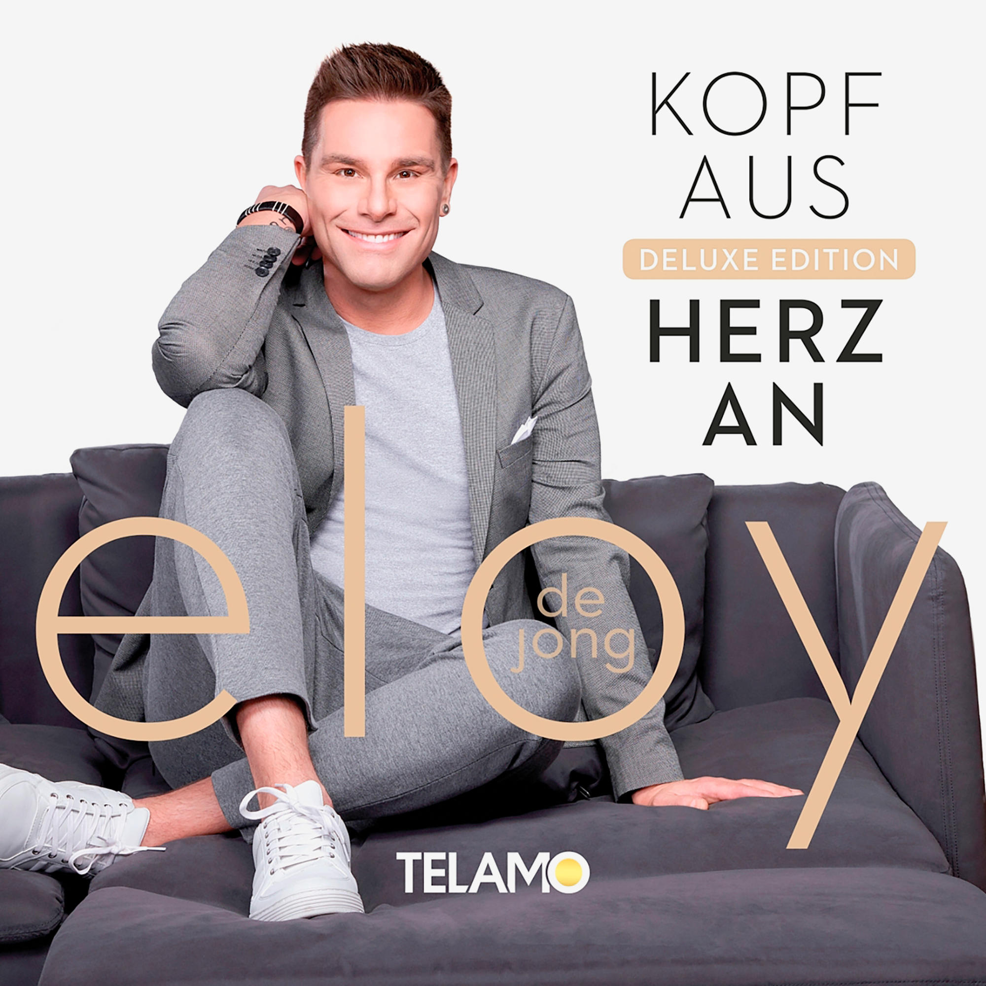 Albumcover von Eloy de Jong, lächelnd auf einem Sofa sitzend, Text sagt 'Kopf Aus Herz An'.