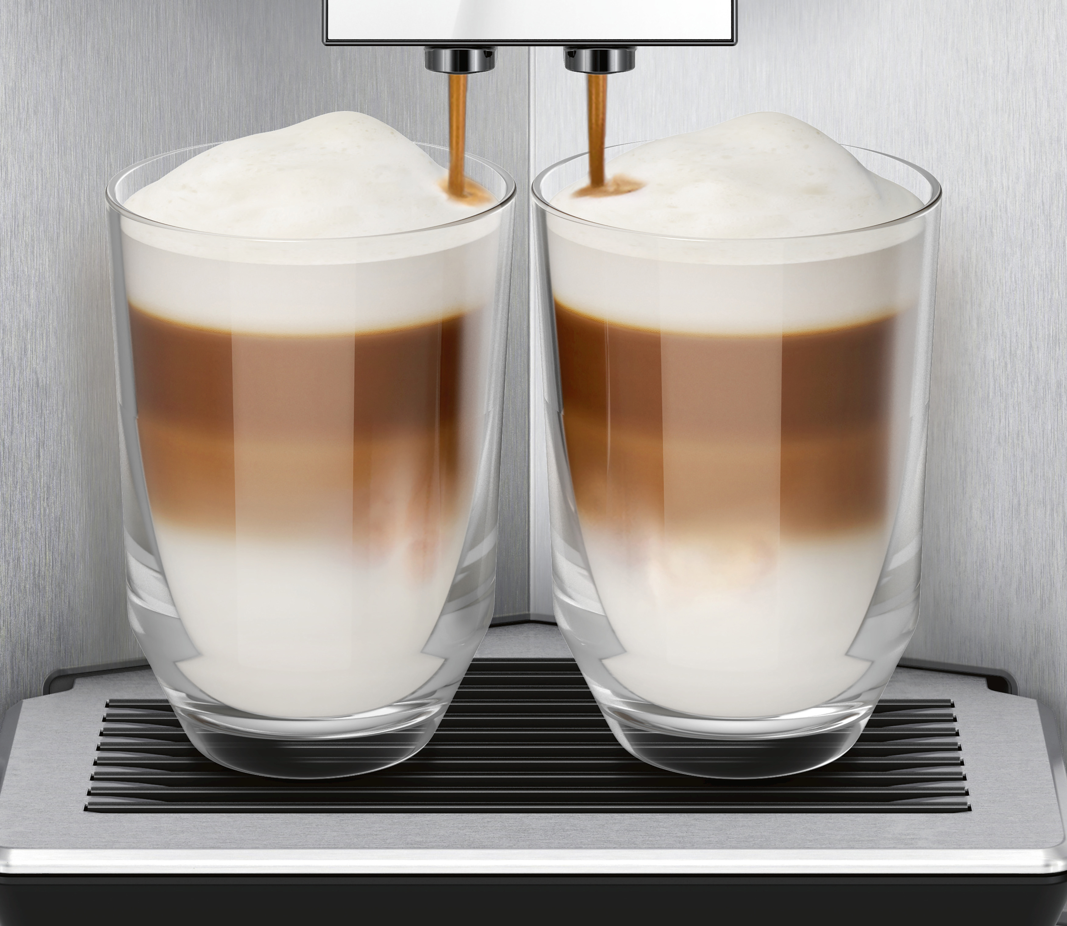 Zwei Gläser geschichteter Latte, die von einer Kaffeemaschine gegossen werden.