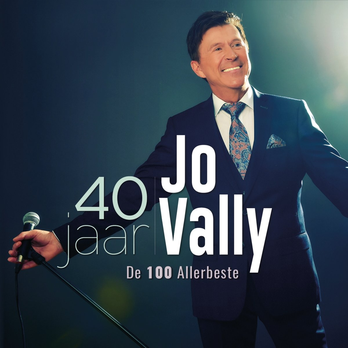 Jo Vally, un homme en costume, tenant un micro, avec le texte '40 jaar Jo Vally'.