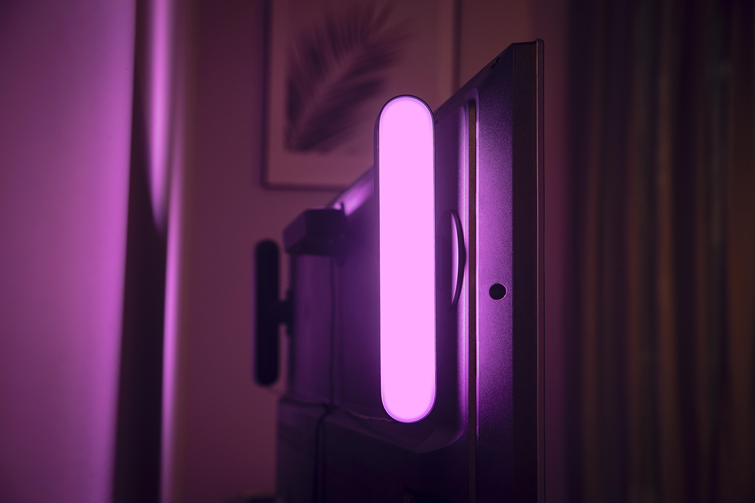 TV with attached, illuminated, vertical light bar, emitting pink light.