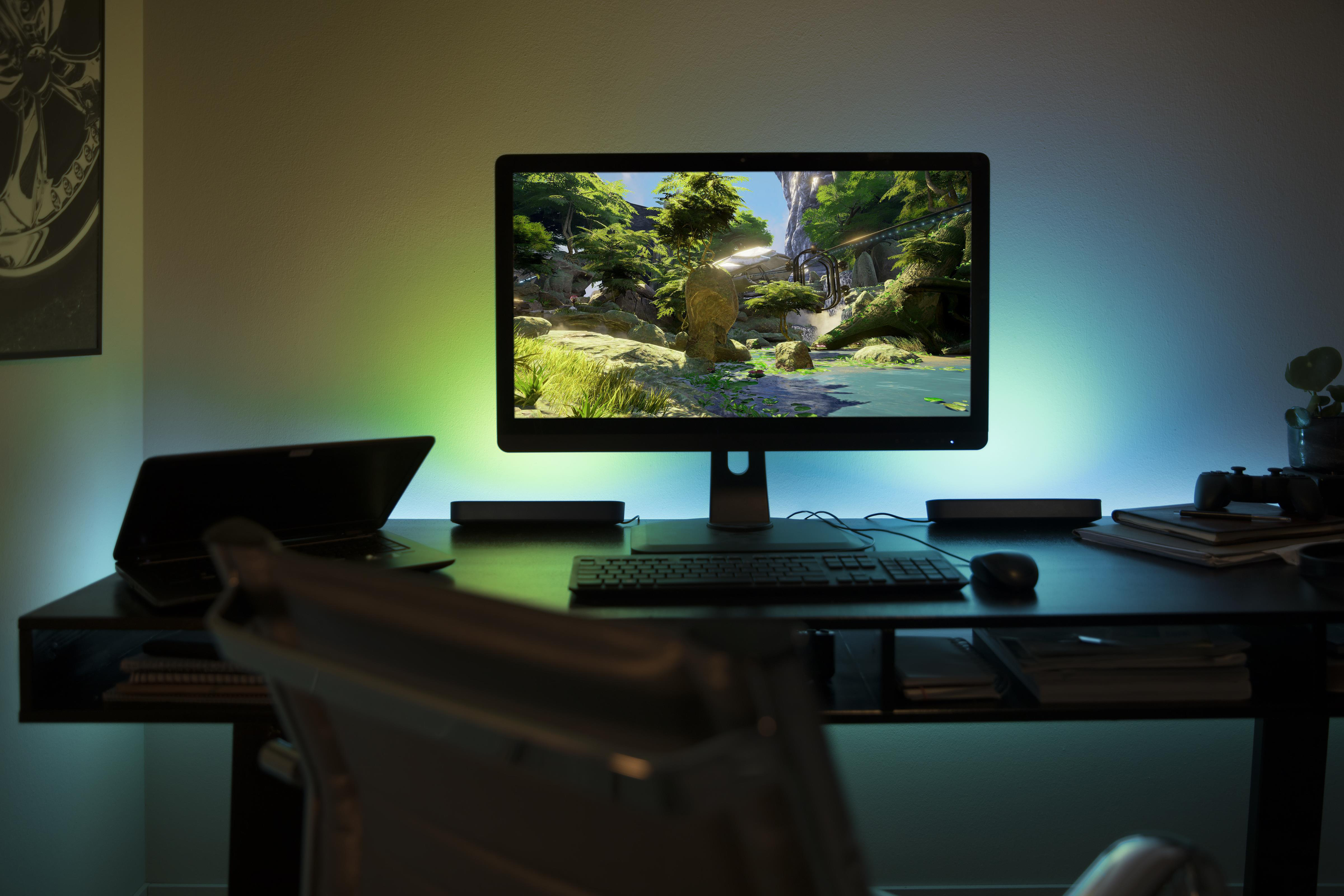A desk setup with a computer screen showing a game scene, laptop, keyboard, and a mouse.