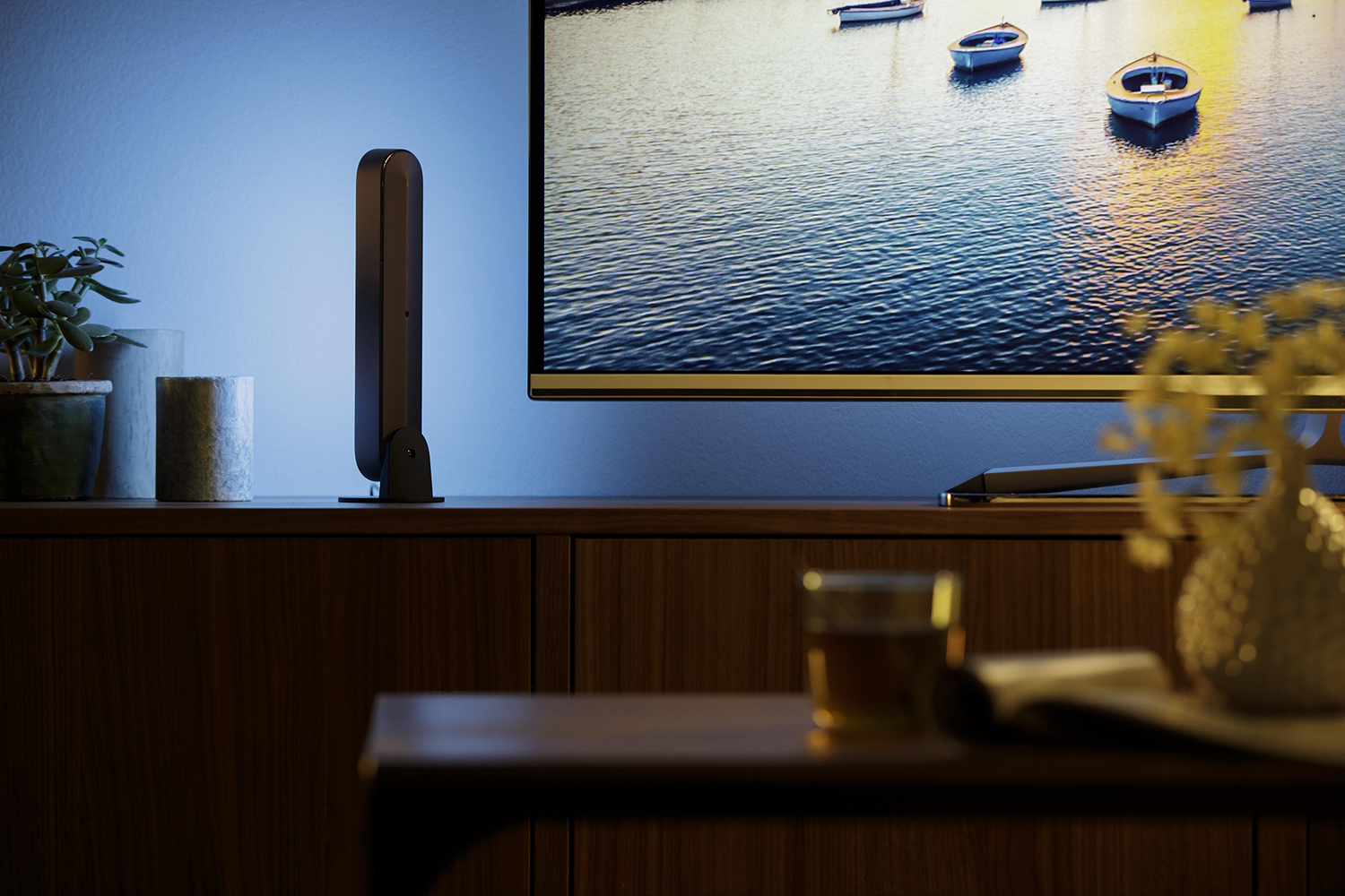 A TV screen showing boats on water, with a black Philips Hue light strip and wooden table.
