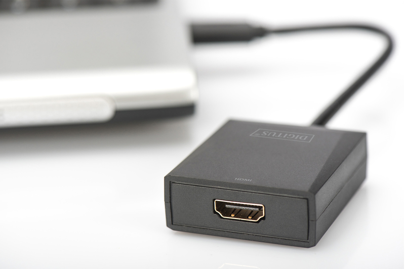 Schwarzer HDMI-Adapter, an einen Laptop angeschlossen. HDMI-Anschluss am Adapter sichtbar. Weißer Hintergrund.