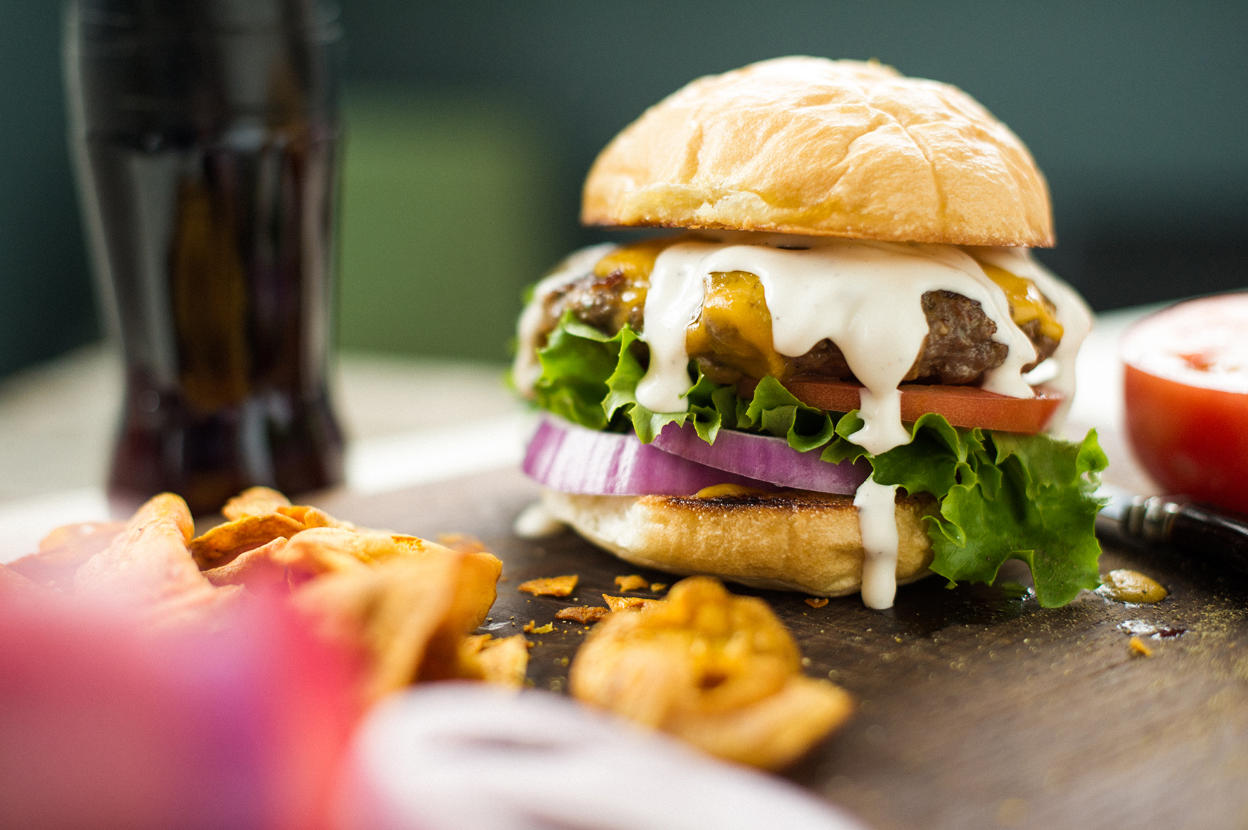 Szezámmagos zsemlével, salátával, sajttal, hagymával és szósszal készült hamburger fából készült deszkán.