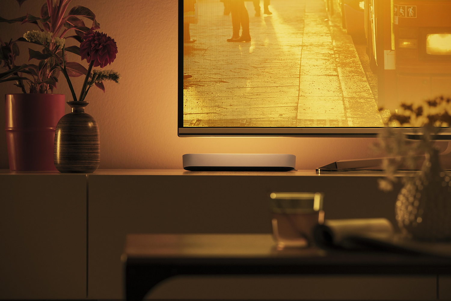Lit light bar below a TV, with blurred figures in the background.