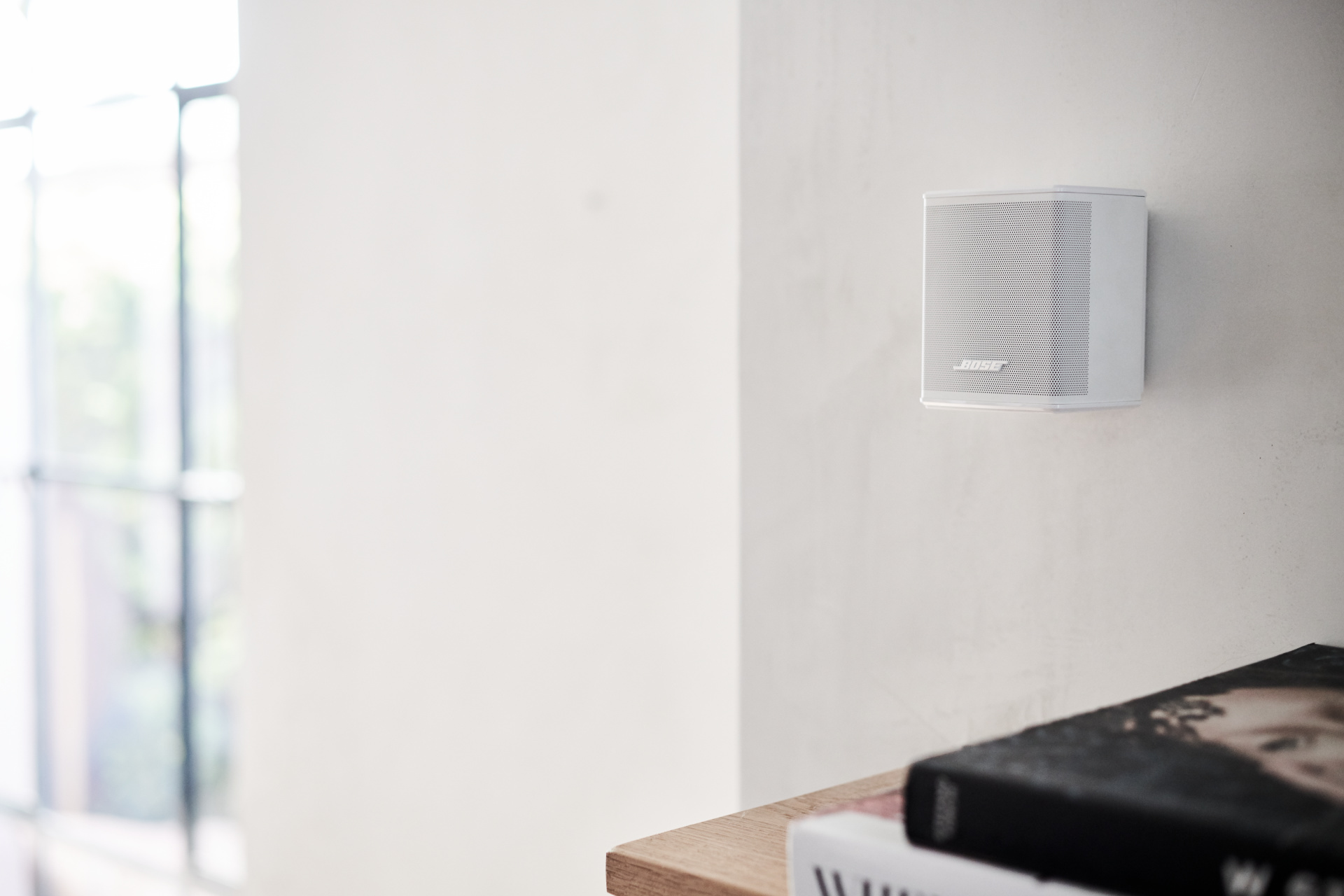 Un haut-parleur blanc monté sur un mur blanc, avec des livres sur une surface en bois en dessous.