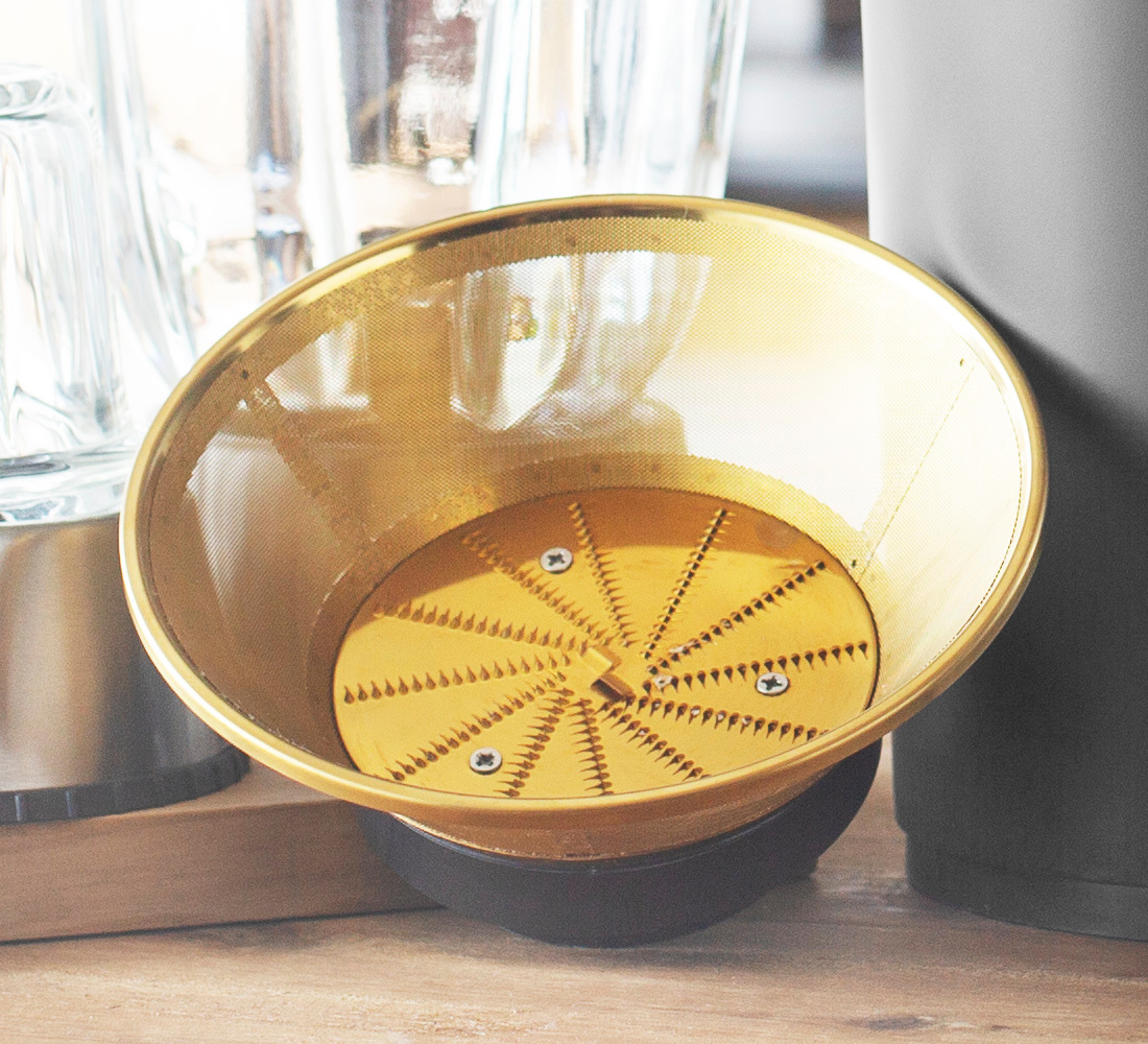 Nahaufnahme eines goldenen Entsafterfilters mit Maschendesign. Der Filter sitzt auf einem schwarzen Sockel.