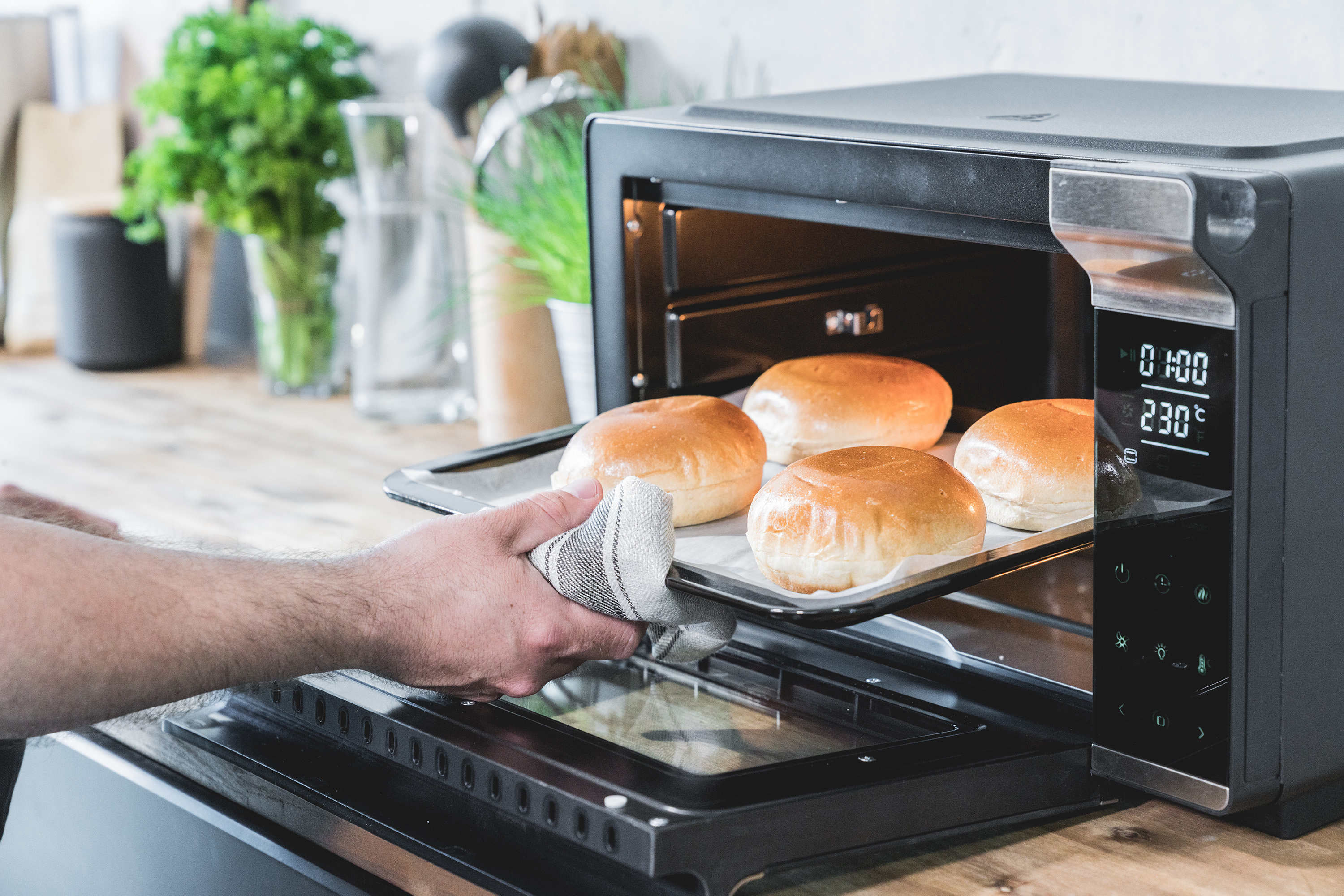 Eine Person entnimmt ein Blech mit gebackenen Brötchen aus einem schwarzen Ofen.
