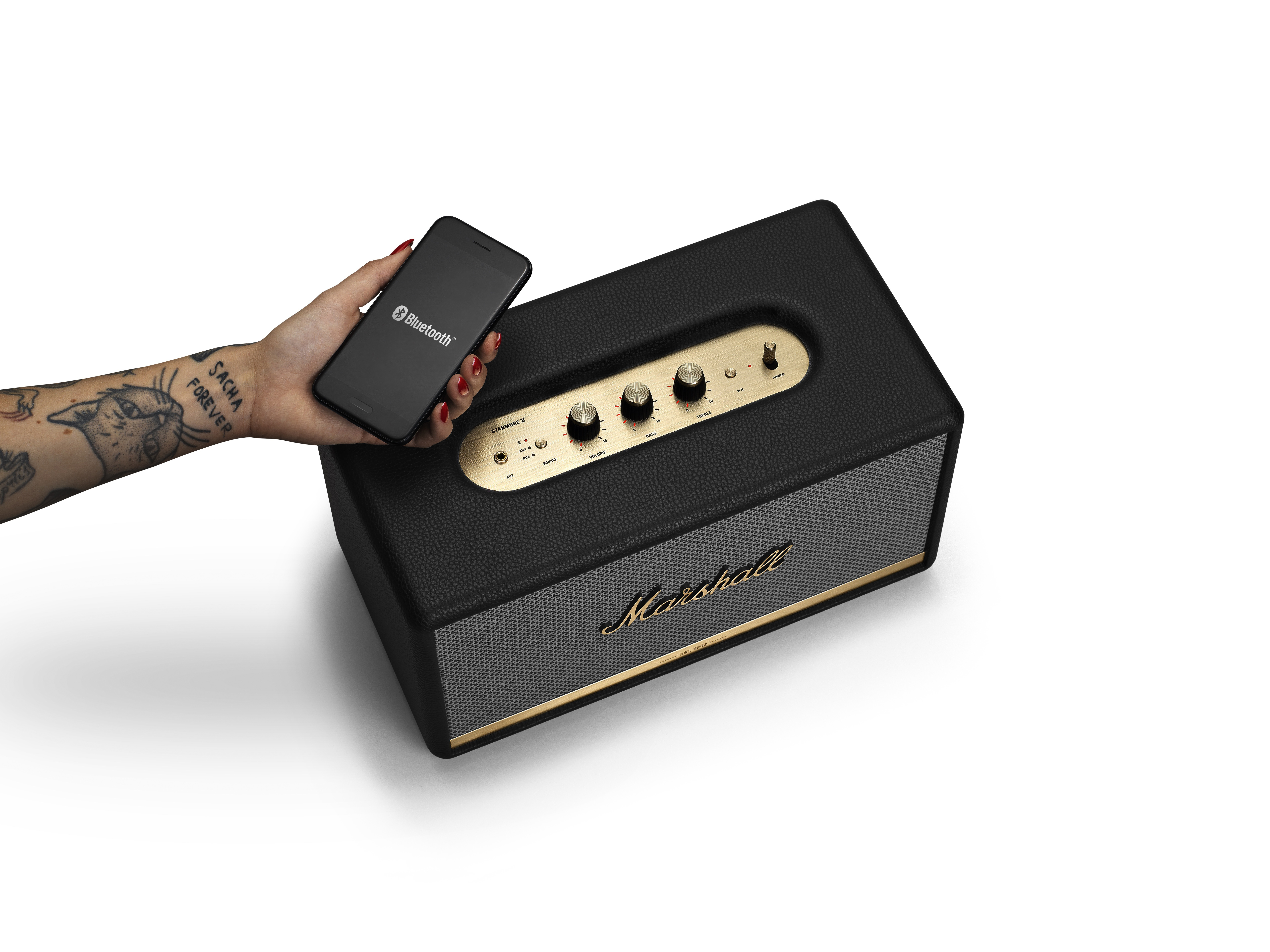 Schwarzer Marshall-Lautsprecher mit goldenen Akzenten, Telefon mit Bluetooth-Verbindung, tätowierter Arm.