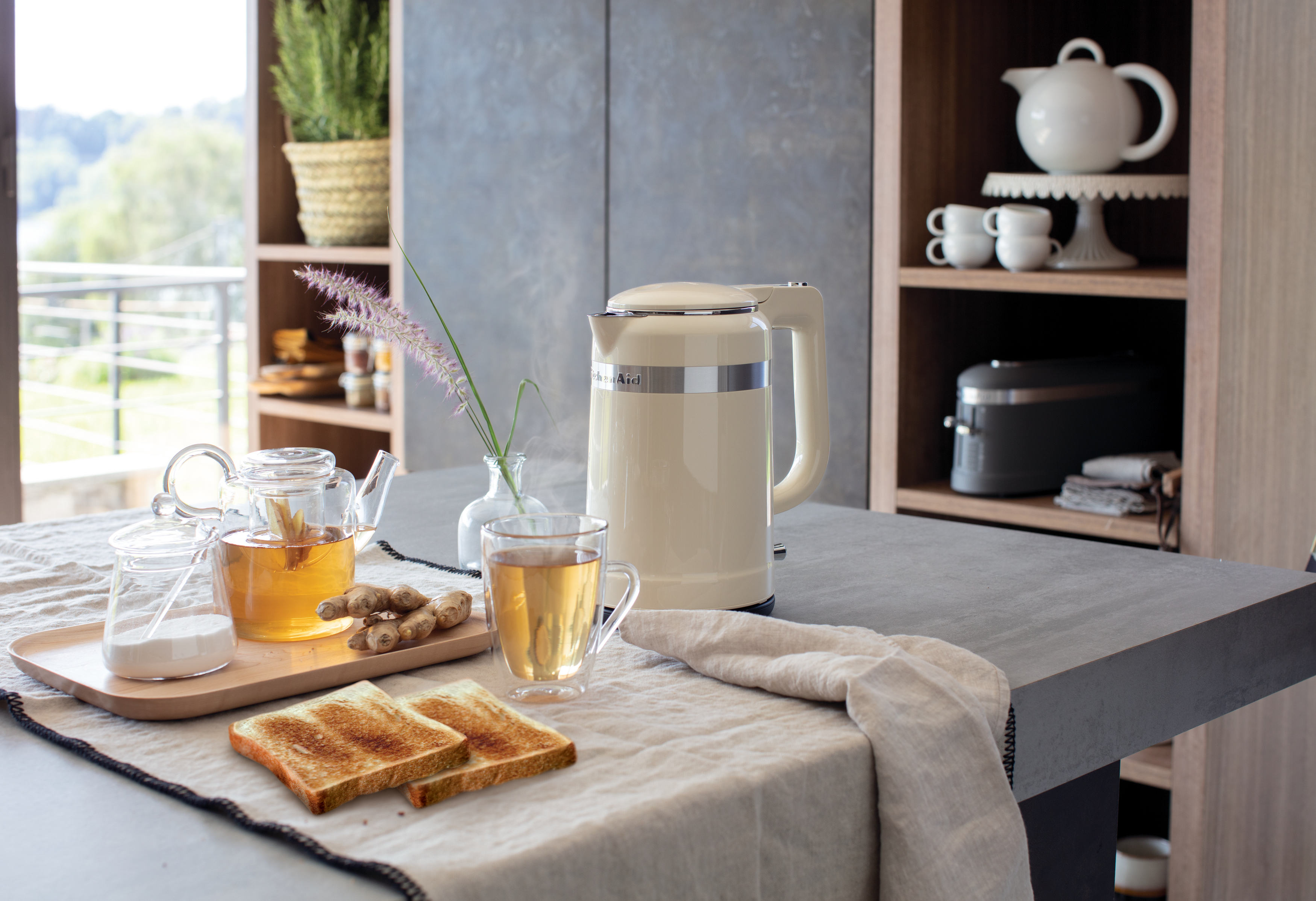 Küchenumgebung mit cremefarbenem Wasserkocher, zwei Toastscheiben und einem Glas Tee.