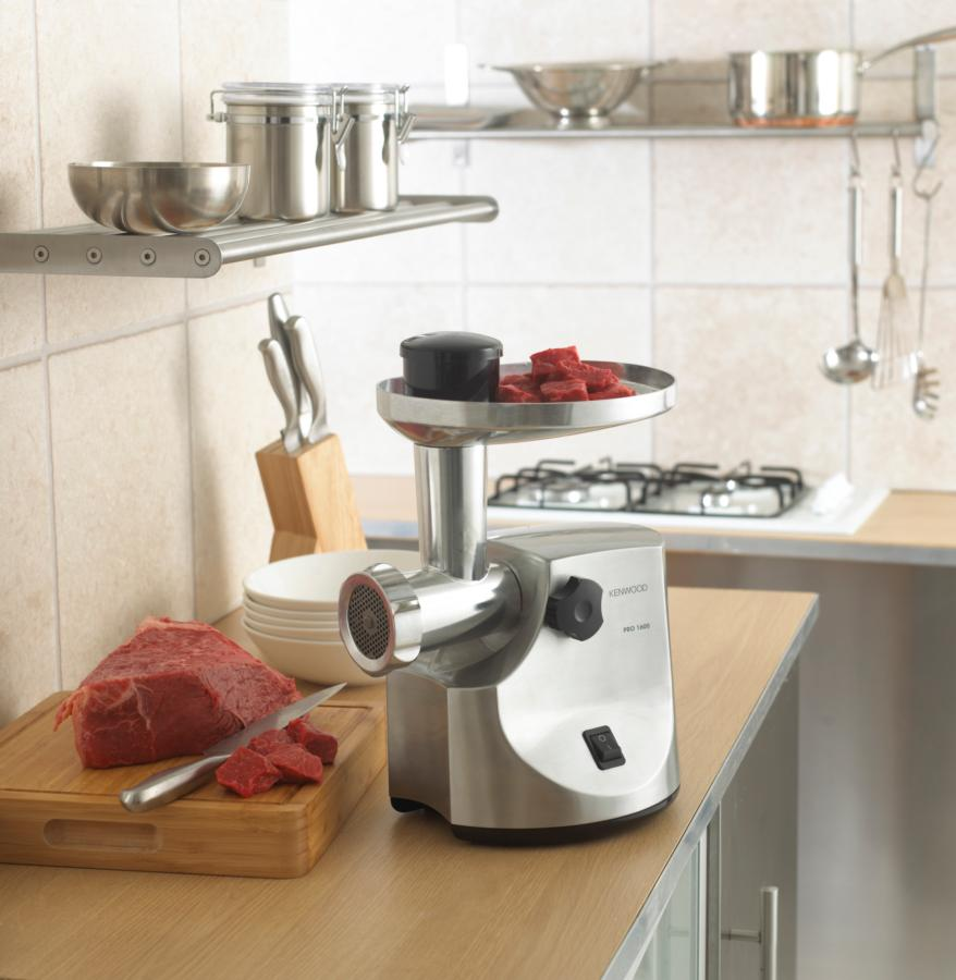 Picadora de carne con carne e ingredientes en una encimera de madera en cocina.