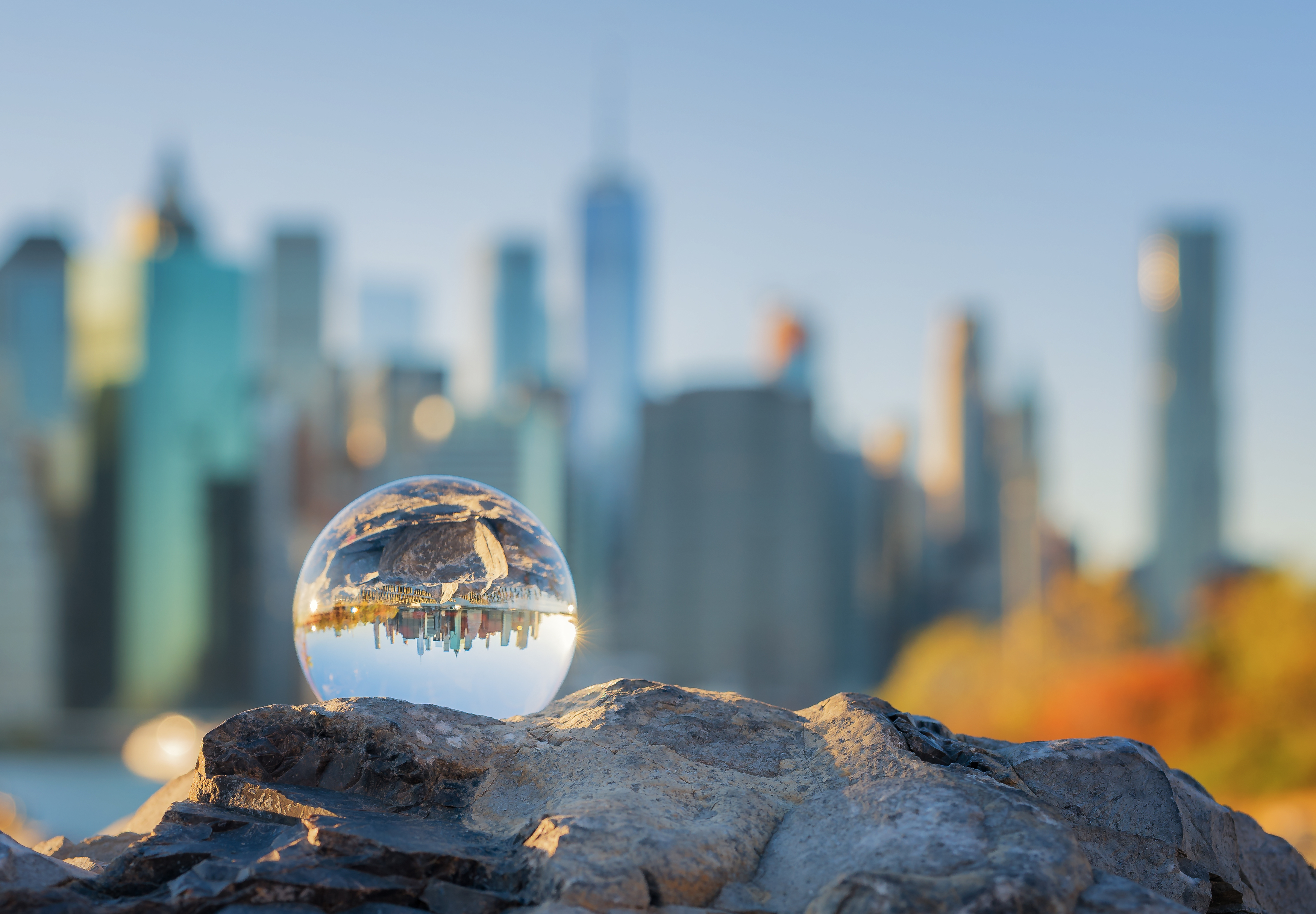 Glaskugel auf Felsen spiegelt Stadtlandschaft, unscharfe Skyline im Hintergrund.