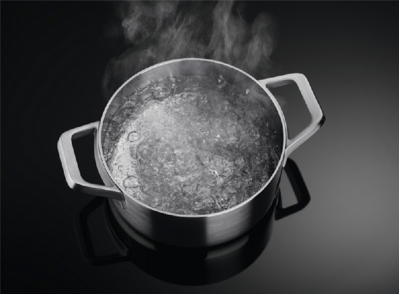 Una olla de acero inoxidable con agua hirviendo. El vapor se eleva del agua sobre una superficie negra.