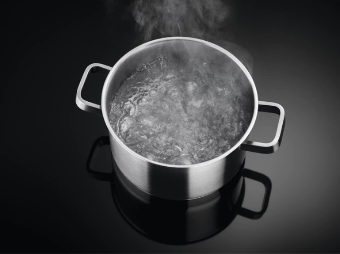Olla de acero inoxidable con agua hirviendo. Vapor ascendiendo.
