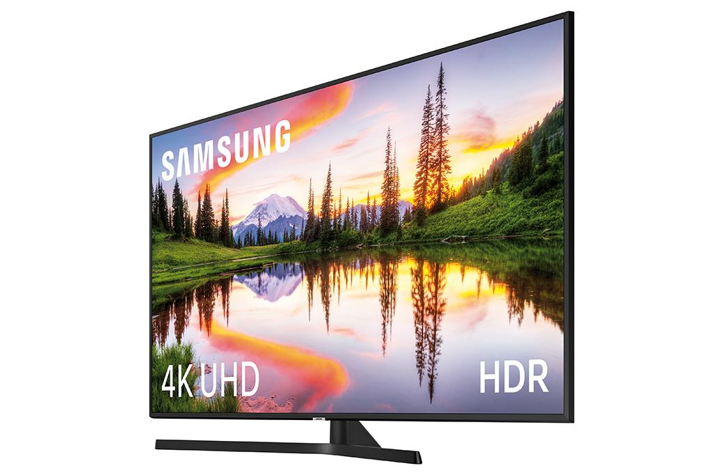 Televisor Samsung grande con un paisaje escénico. La pantalla muestra árboles, cielo y agua. Fondo blanco.