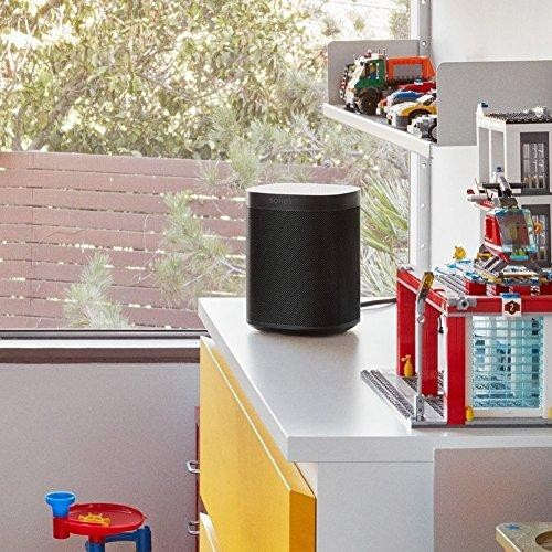 Altavoz negro Sonos sobre una superficie blanca, con juguetes y estanterías en el fondo.