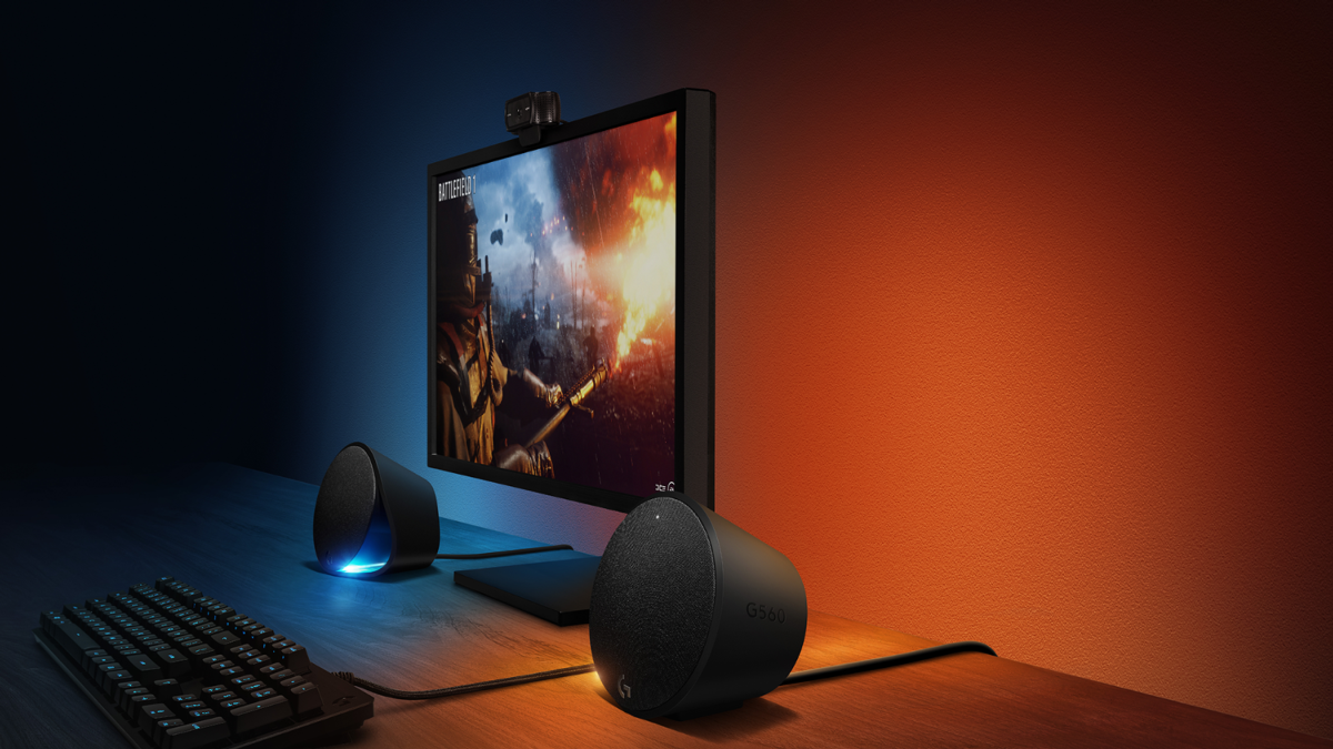 Configuración de juego con monitor, altavoces, teclado. Iluminación naranja y azul.