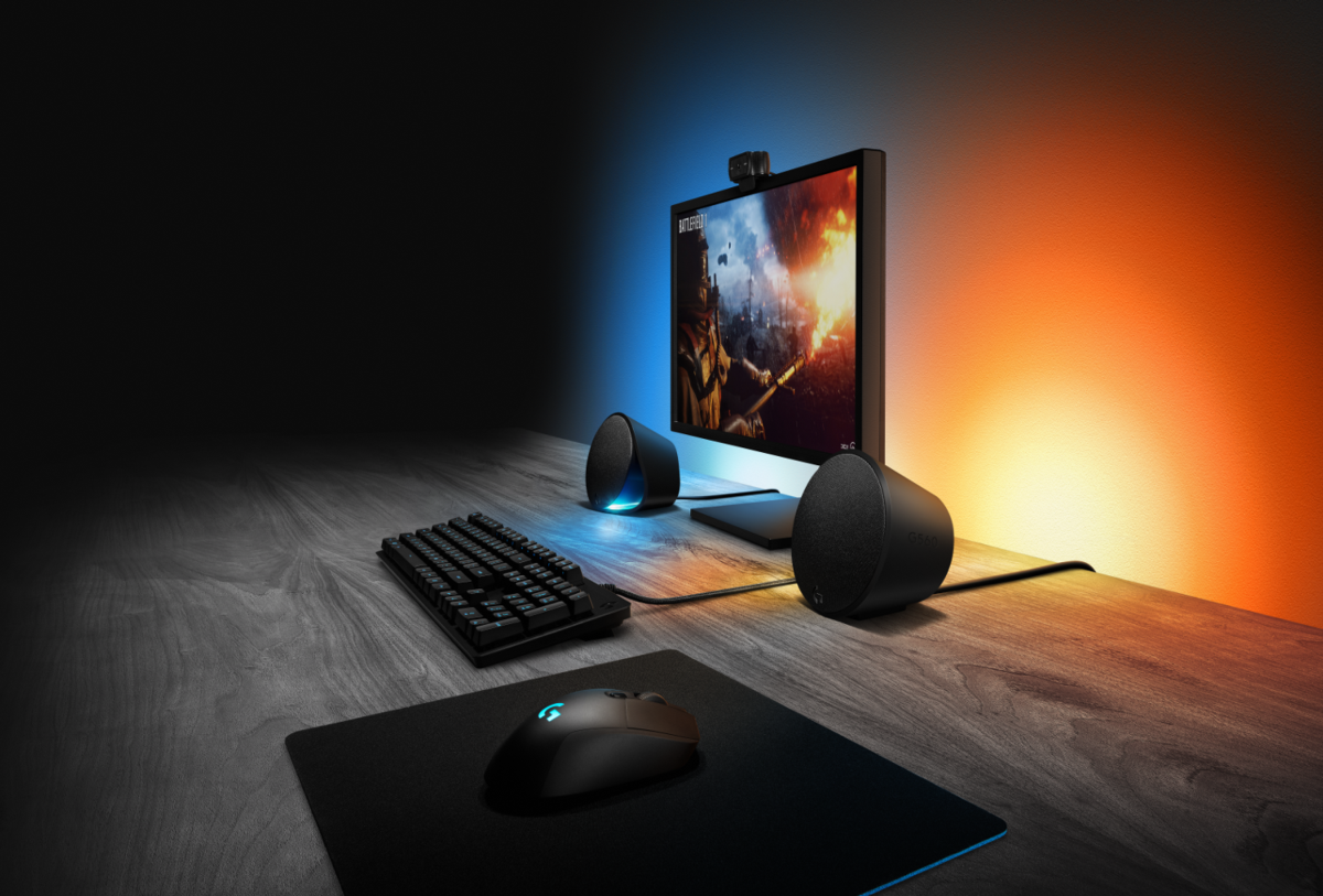 Una configuración de juegos con teclado, ratón, altavoces y monitor en un escritorio de madera con iluminación.