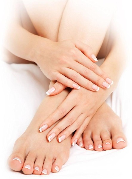Manos y pies de mujer con uñas manicuradas, plegados sobre una sábana blanca.