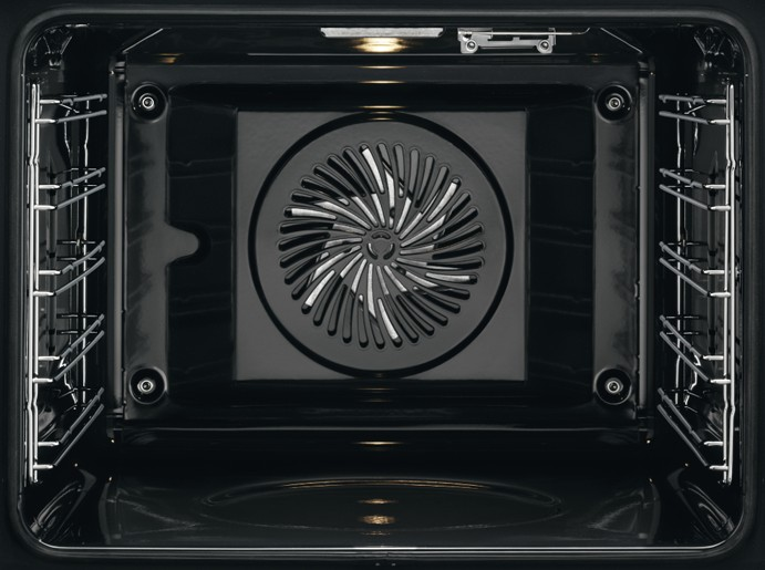 Dentro de un horno negro. Muestra el ventilador del elemento calefactor y las rejillas metálicas.