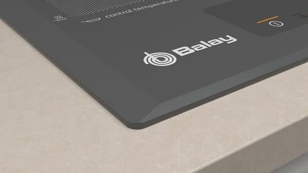 Primer plano de una encimera negra integrada con logotipo Balay y controles táctiles sobre encimera crema.