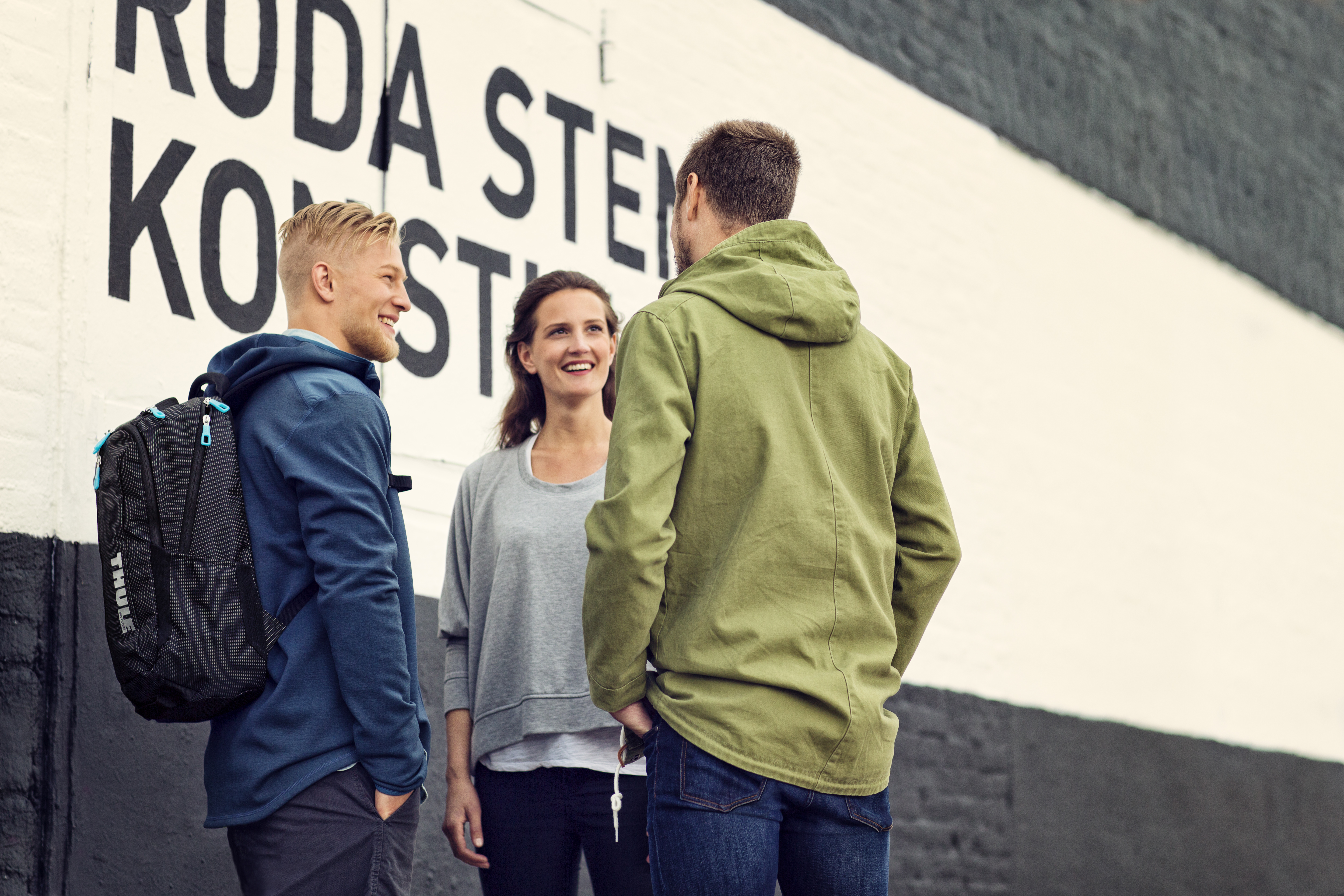 Tres personas hablando frente a una pared con texto negro.