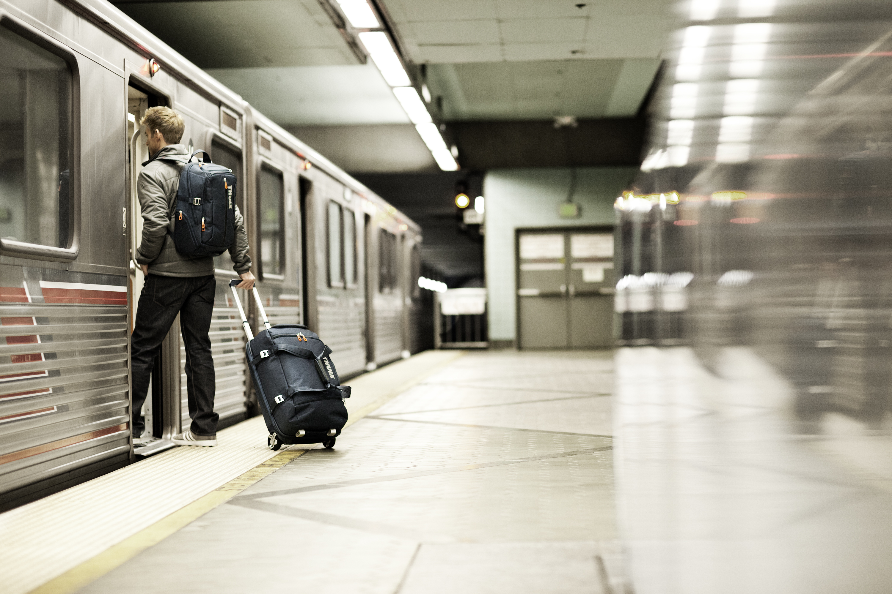 Una persona con una mochila y una maleta con ruedas entrando a un tren en una estación de metro.