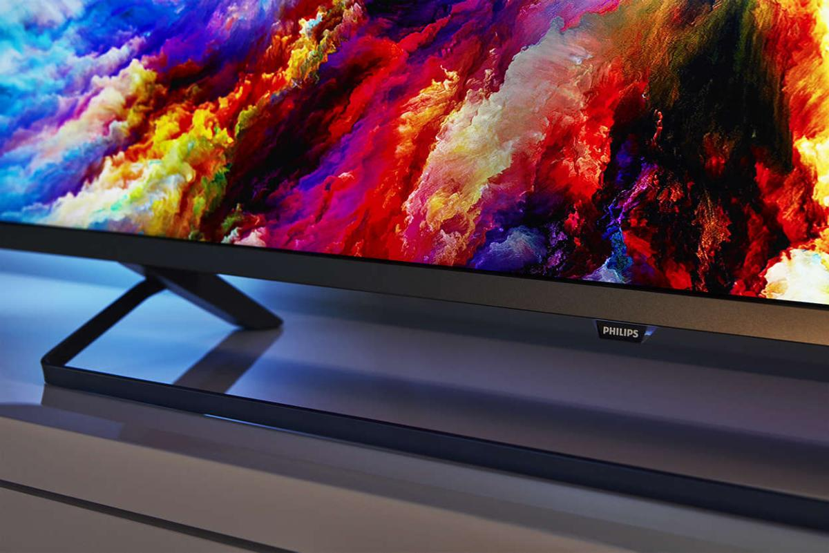 Primer plano de un televisor que muestra arte abstracto colorido, con un soporte negro sobre una superficie blanca.