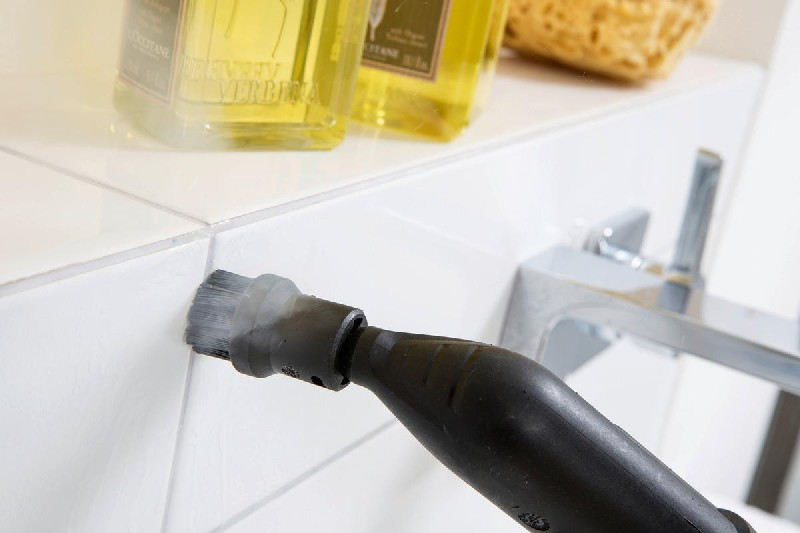 Limpieza de una pared de azulejos blancos con vapor. Se utiliza una herramienta de limpieza negra para frotar.