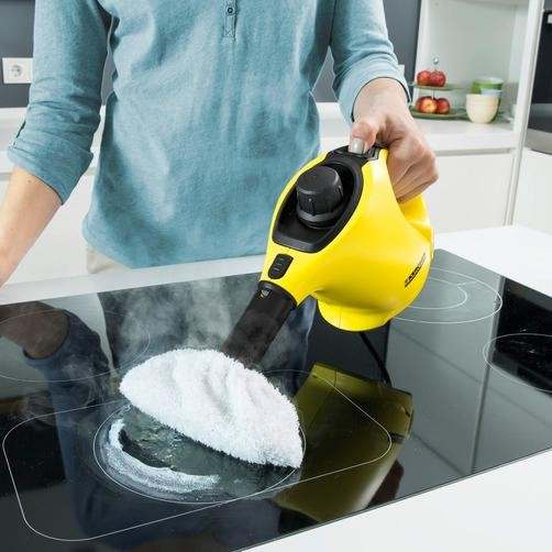 Persona limpiando una encimera negra con un vaporizador de mano amarillo.