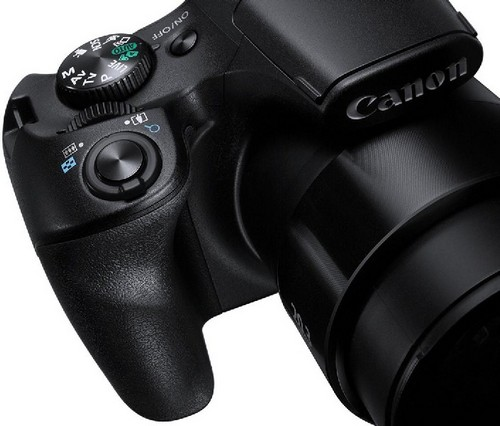 Cámara Canon negra con objetivo zoom. La parte superior tiene controles y el logotipo de Canon. Negro con detalles grises.