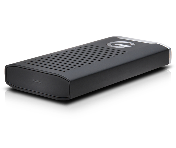 Disco duro externo negro G-Technology, forma rectangular con parte superior plateada, sobre superficie blanca.