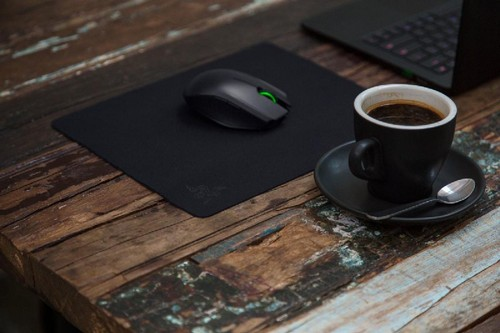 Taza de café y ratón en un escritorio de madera. Portátil en el fondo. El escritorio tiene una alfombrilla.