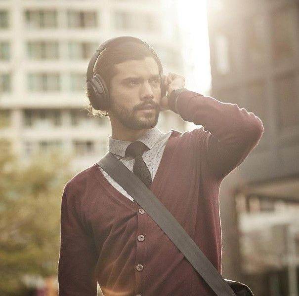 Un hombre con auriculares, traje, sosteniendo un auricular. Edificios de la ciudad en el fondo.