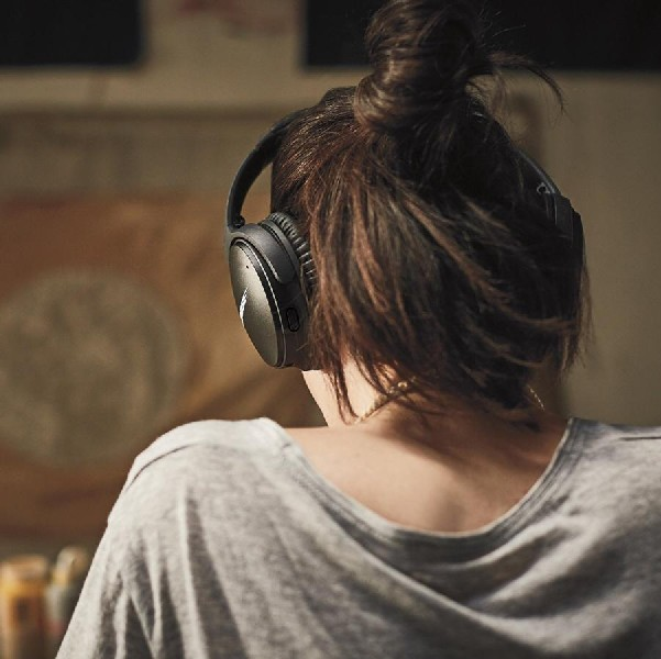 Una mujer con camisa gris y auriculares negros, vista desde atrás. Su cabello está recogido en un moño.