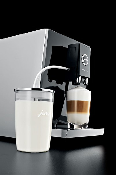 Una cafetera con un recipiente de leche, preparando un café en capas en un vaso.