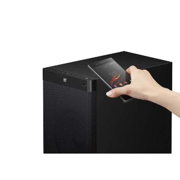 Una mano sosteniendo un teléfono hacia un altavoz negro. El altavoz tiene una etiqueta BT.