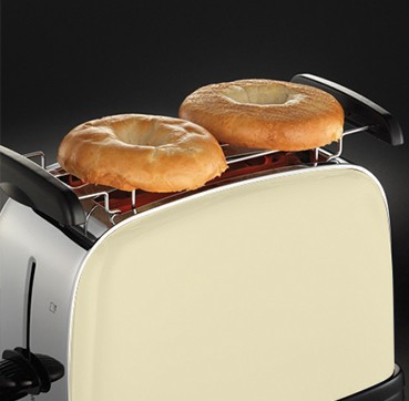 Primer plano de una tostadora con dos bagels tostados encima, color crema.