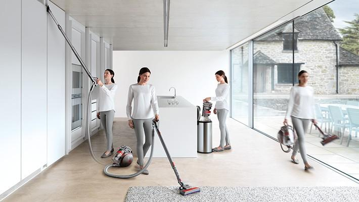 Cuatro mujeres aspirando una habitación con una aspiradora Dyson. Ropa blanca y gris.