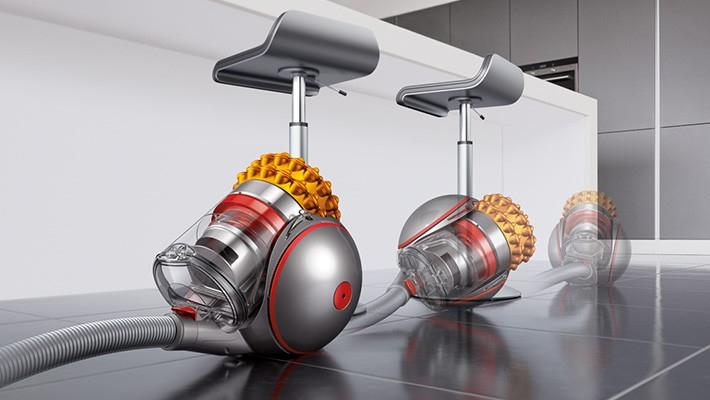 Tres aspiradoras Dyson, dos con taburetes, en un suelo brillante, en un entorno de cocina moderno.